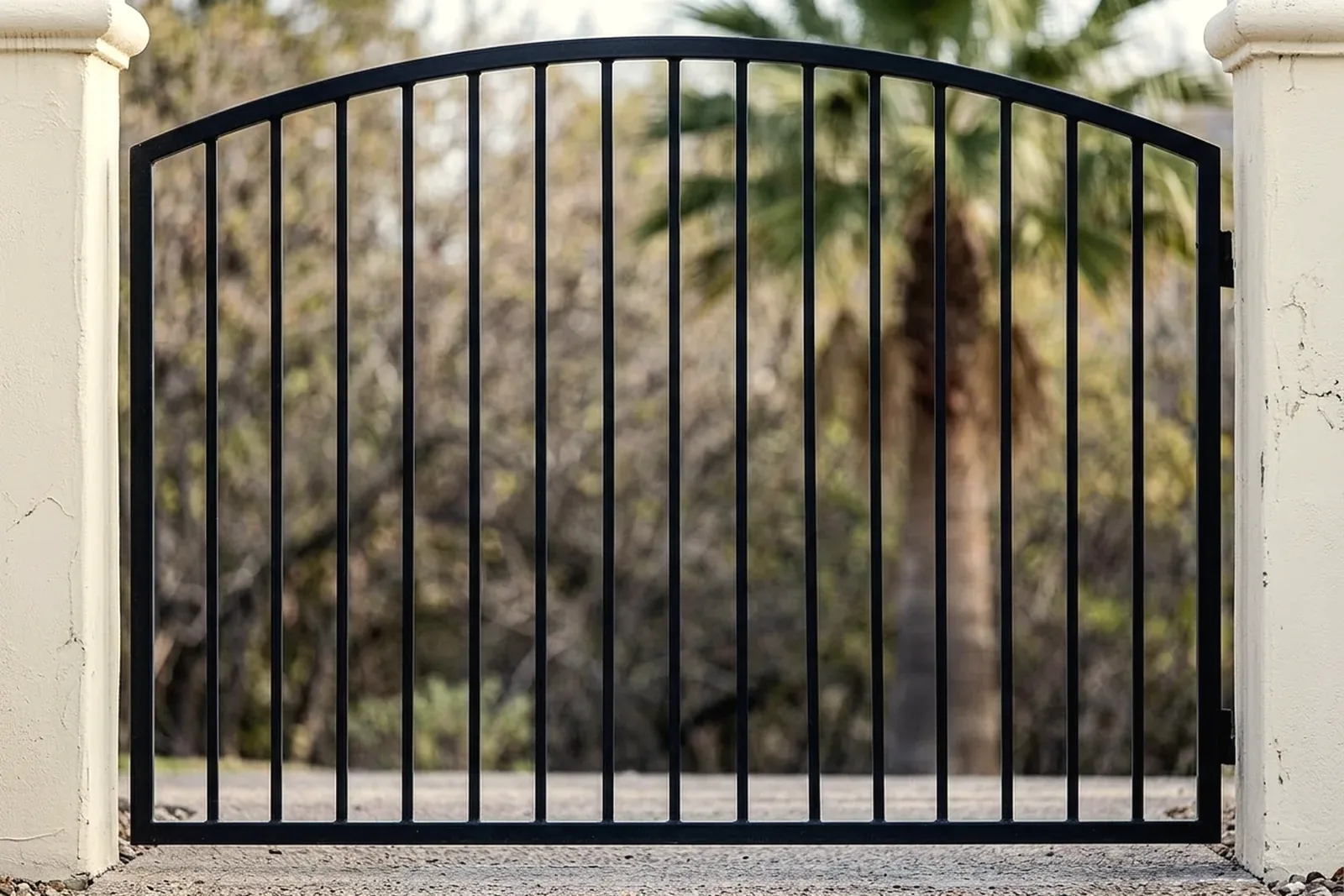 Custom black iron double driveway gate between stucco pillars